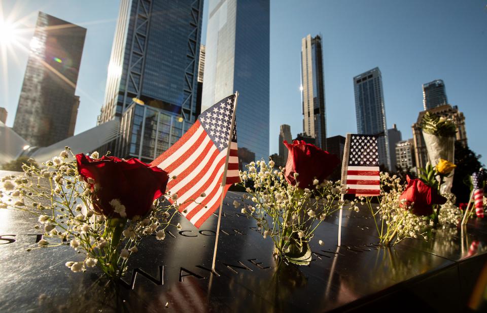 Bright sunshine illuminates the Memorial, which is decorated with American flags and flowers.