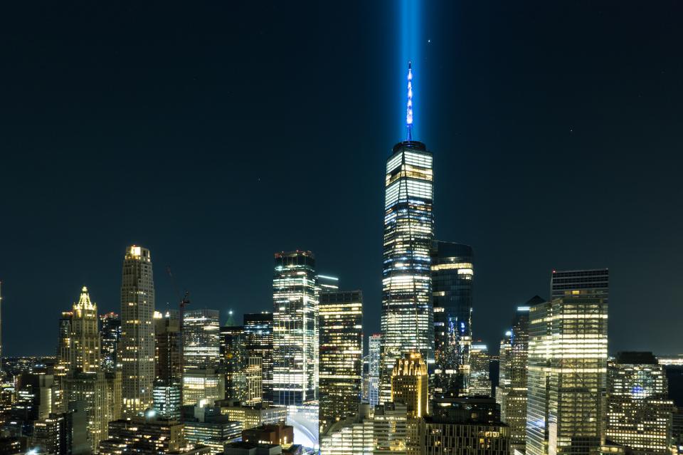 Two beams of blue light emanate from the top of One World Trade Center, against a dark sky