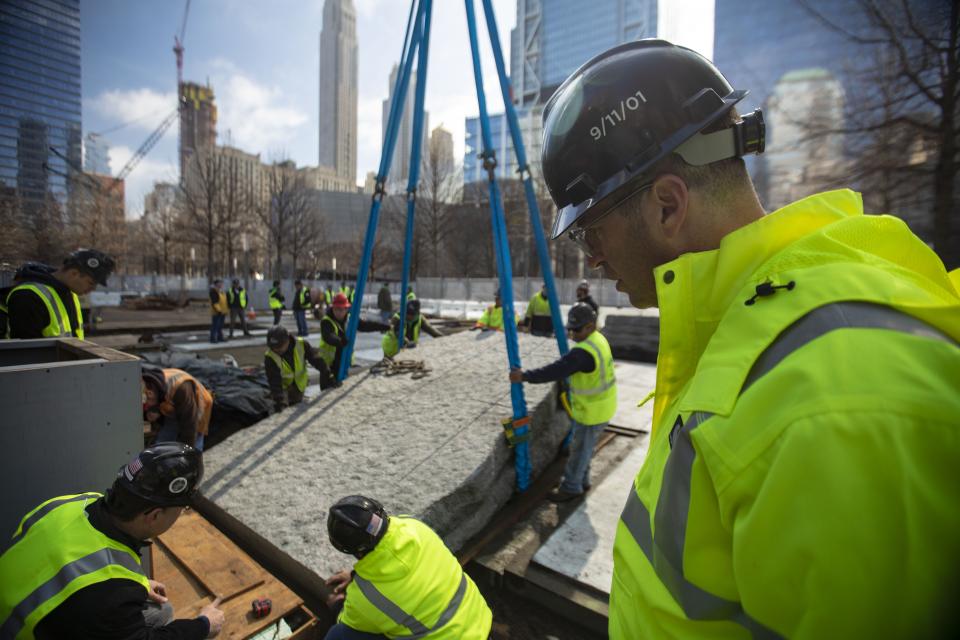 Construction workers in neon yellow gear install a large stone monolith at the Memorial